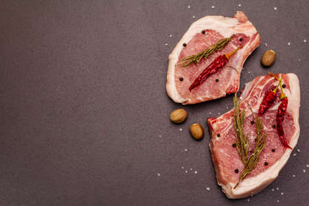 Raw pork steaks on trendy black stone concrete background. Spices, sea salt, rosemary, chili pepper, top view, copy spaceの写真素材