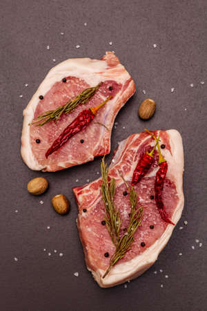 Raw pork steaks on trendy black stone concrete background. Spices, sea salt, rosemary, chili pepper, top viewの写真素材