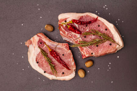 Raw pork steaks on trendy black stone concrete background. Spices, sea salt, rosemary, chili pepper, top viewの写真素材