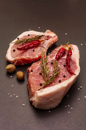 Raw pork steaks on trendy black stone concrete background. Spices, sea salt, rosemary, chili pepper, close upの写真素材