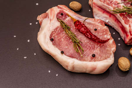 Raw pork steaks on trendy black stone concrete background. Spices, sea salt, rosemary, chili pepper, close upの写真素材