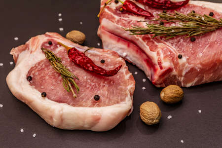 Raw pork steaks on trendy black stone concrete background. Spices, sea salt, rosemary, chili pepper, close upの写真素材
