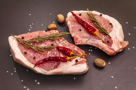 Raw pork steaks on trendy black stone concrete background. Spices, sea salt, rosemary, chili pepper, top viewの写真素材