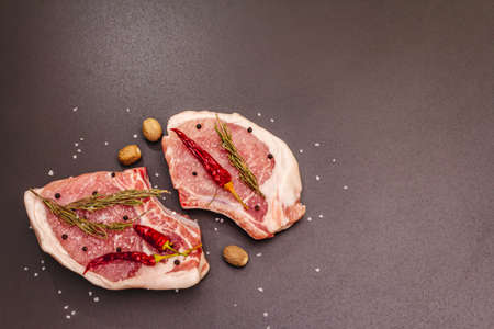 Raw pork steaks on trendy black stone concrete background. Spices, sea salt, rosemary, chili pepper, top view, copy spaceの写真素材