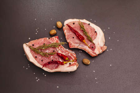 Raw pork steaks on trendy black stone concrete background. Spices, sea salt, rosemary, chili pepper, top view, copy spaceの写真素材