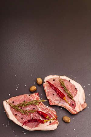Raw pork steaks on trendy black stone concrete background. Spices, sea salt, rosemary, chili pepper, top view, copy spaceの写真素材