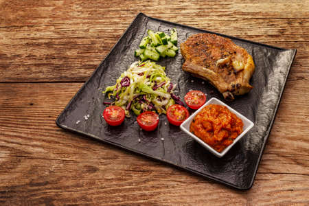 Grilled pork steak. Cole slow salad, tomato sauce, fresh vegetables. Old wooden tableの写真素材