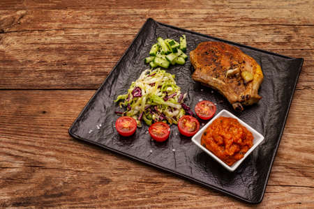 Grilled pork steak. Cole slow salad, tomato sauce, fresh vegetables. Old wooden tableの写真素材