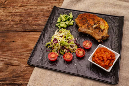 Grilled pork steak. Cole slow salad, tomato sauce, fresh vegetables. Old wooden tableの写真素材