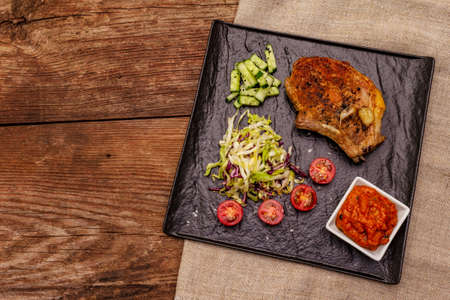 Grilled pork steak. Cole slow salad, tomato sauce, fresh vegetables. Old wooden table, top viewの写真素材