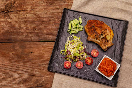 Grilled pork steak. Cole slow salad, tomato sauce, fresh vegetables. Old wooden table, top viewの写真素材