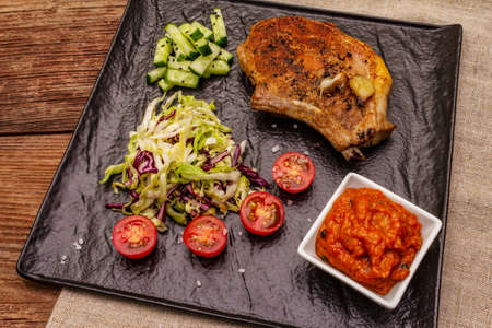 Grilled pork steak. Cole slow salad, tomato sauce, fresh vegetables. Old wooden tableの写真素材