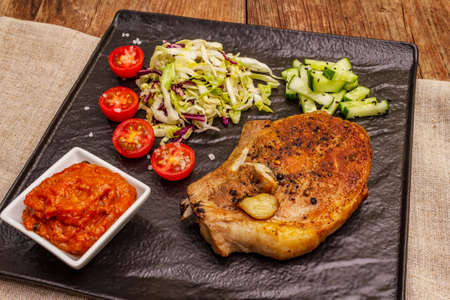 Grilled pork steak. Cole slow salad, tomato sauce, fresh vegetables. Old wooden tableの写真素材