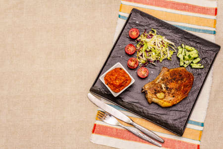 Grilled pork steak. Cole slow salad, tomato sauce, fresh vegetables. Beige table background, top viewの写真素材