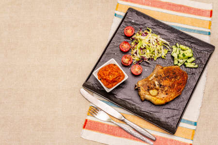 Grilled pork steak. Cole slow salad, tomato sauce, fresh vegetables. Beige table background, top viewの写真素材