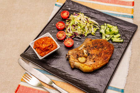 Grilled pork steak. Cole slow salad, tomato sauce, fresh vegetables. Beige table backgroundの写真素材