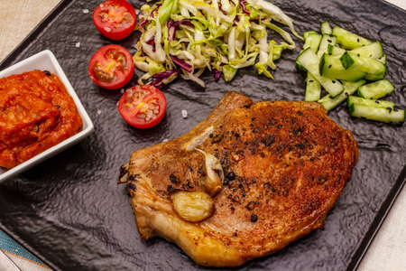 Grilled pork steak. Cole slow salad, tomato sauce, fresh vegetables. Beige table background, close upの写真素材