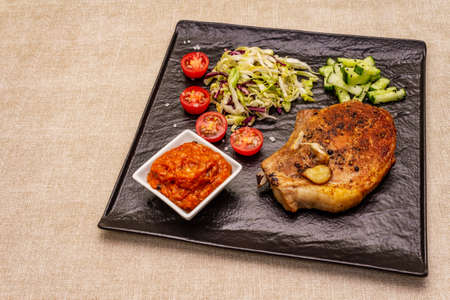 Grilled pork steak. Cole slow salad, tomato sauce, fresh vegetables. Beige table backgroundの写真素材