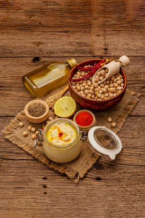 Hummus on old wooden boards background. Dry chickpea, olive oil, lemon, cumin and chili pepper. Traditional food in Middle Eastern and Mediterranean cuisineの写真素材