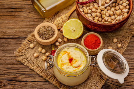 Hummus on old wooden boards background. Dry chickpea, olive oil, lemon, cumin and chili pepper. Traditional food in Middle Eastern and Mediterranean cuisine, top viewの写真素材