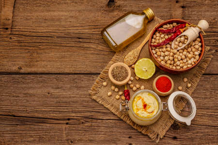 Hummus on old wooden boards background. Dry chickpea, olive oil, lemon, cumin and chili pepper. Traditional food in Middle Eastern and Mediterranean cuisine, copy spaceの写真素材
