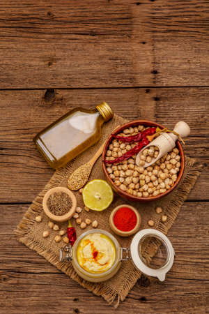 Hummus on old wooden boards background. Dry chickpea, olive oil, lemon, cumin and chili pepper. Traditional food in Middle Eastern and Mediterranean cuisine, top viewの写真素材