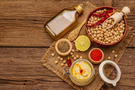 Hummus on old wooden boards background. Dry chickpea, olive oil, lemon, cumin and chili pepper. Traditional food in Middle Eastern and Mediterranean cuisine, copy spaceの写真素材