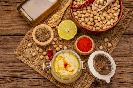 Hummus on old wooden boards background. Dry chickpea, olive oil, lemon, cumin and chili pepper. Traditional food in Middle Eastern and Mediterranean cuisine, top viewの写真素材