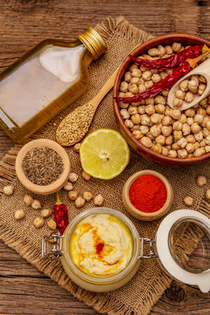 Hummus on old wooden boards background. Dry chickpea, olive oil, lemon, cumin and chili pepper. Traditional food in Middle Eastern and Mediterranean cuisine, top viewの写真素材