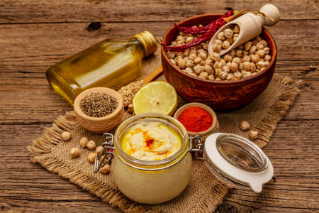 Hummus on old wooden boards background. Dry chickpea, olive oil, lemon, cumin and chili pepper. Traditional food in Middle Eastern and Mediterranean cuisine, close upの写真素材