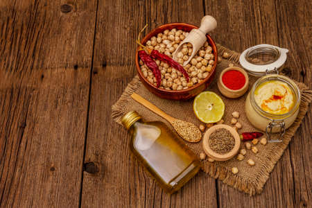 Hummus on old wooden boards background. Dry chickpea, olive oil, lemon, cumin and chili pepper. Traditional food in Middle Eastern and Mediterranean cuisine, copy spaceの写真素材