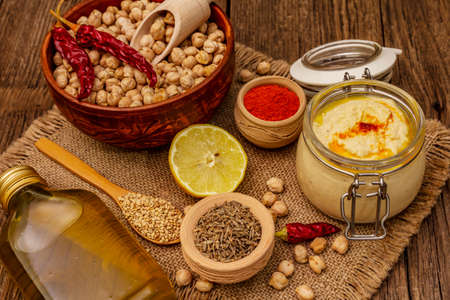 Hummus on old wooden boards background. Dry chickpea, olive oil, lemon, cumin and chili pepper. Traditional food in Middle Eastern and Mediterranean cuisine, close upの写真素材
