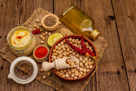 Hummus on old wooden boards background. Dry chickpea, olive oil, lemon, cumin and chili pepper. Traditional food in Middle Eastern and Mediterranean cuisine, top viewの写真素材
