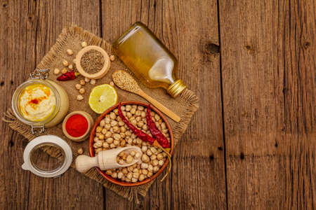 Hummus on old wooden boards background. Dry chickpea, olive oil, lemon, cumin and chili pepper. Traditional food in Middle Eastern and Mediterranean cuisine, copy spaceの写真素材