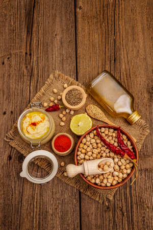 Hummus on old wooden boards background. Dry chickpea, olive oil, lemon, cumin and chili pepper. Traditional food in Middle Eastern and Mediterranean cuisine, copy spaceの写真素材