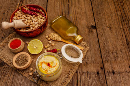 Hummus on old wooden boards background. Dry chickpea, olive oil, lemon, cumin and chili pepper. Traditional food in Middle Eastern and Mediterranean cuisine, copy spaceの写真素材