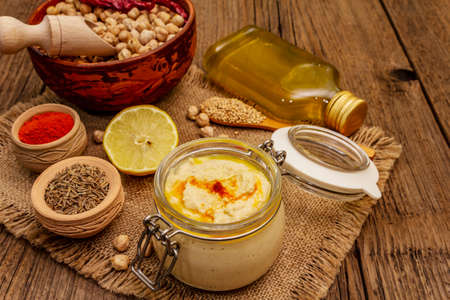 Hummus on old wooden boards background. Dry chickpea, olive oil, lemon, cumin and chili pepper. Traditional food in Middle Eastern and Mediterranean cuisine, close upの写真素材