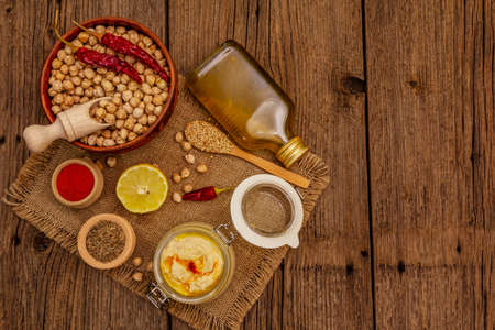 Hummus on old wooden boards background. Dry chickpea, olive oil, lemon, cumin and chili pepper. Traditional food in Middle Eastern and Mediterranean cuisine, copy spaceの写真素材