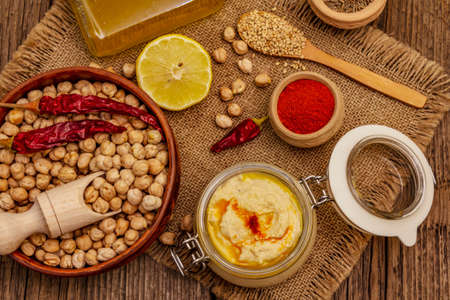 Hummus on old wooden boards background. Dry chickpea, olive oil, lemon, cumin and chili pepper. Traditional food in Middle Eastern and Mediterranean cuisine, top viewの写真素材