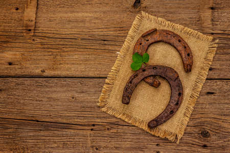 Two very old cast iron metal horse horseshoes, fresh clover leaf. Good luck symbol, St.Patrick's Day concept. Antique wooden background, horse accessoriesの写真素材