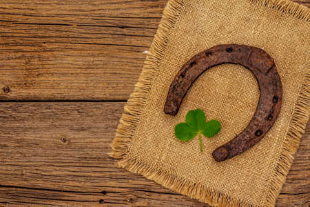 Very old cast iron metal horse horseshoe, fresh clover leaf. Good luck symbol, St.Patrick's Day concept. Antique wooden background, horse accessoriesの写真素材