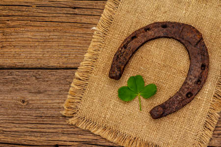 Very old cast iron metal horse horseshoe, fresh clover leaf. Good luck symbol, St.Patrick's Day concept. Antique wooden background, horse accessoriesの写真素材