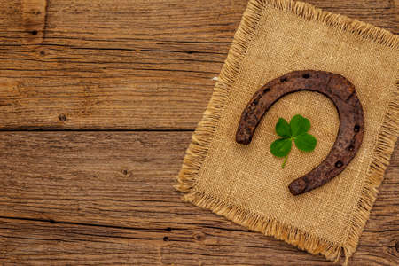 Very old cast iron metal horse horseshoe, fresh clover leaf. Good luck symbol, St.Patrick's Day concept. Antique wooden background, horse accessoriesの写真素材