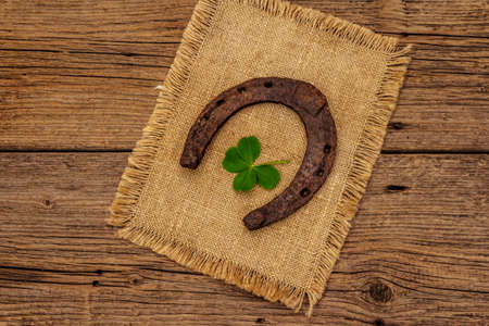 Very old cast iron metal horse horseshoe, fresh clover leaf. Good luck symbol, St.Patrick's Day concept. Antique wooden background, horse accessoriesの写真素材