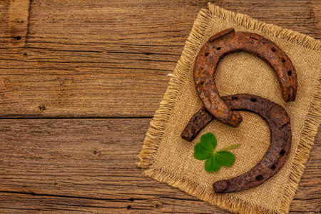 Two very old cast iron metal horse horseshoes, fresh clover leaf. Good luck symbol, St.Patrick's Day concept. Antique wooden background, horse accessoriesの写真素材