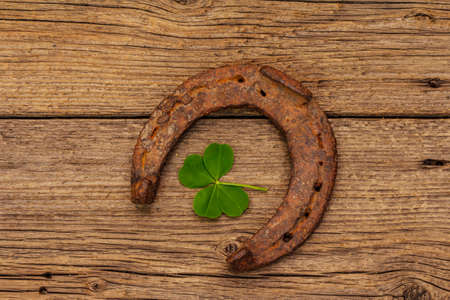 Very old cast iron metal horse horseshoe, fresh clover leaf. Good luck symbol, St.Patrick's Day concept. Antique wooden background, horse accessoriesの写真素材