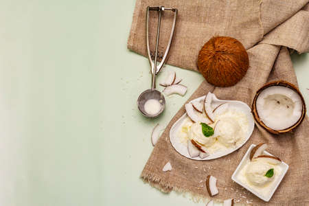 Lactose free coconut ice cream. Special spoon, halves of fruit, flakes. Vegan dessert concept. Light green background, top viewの写真素材