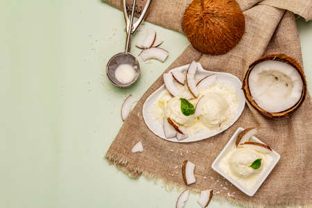 Lactose free coconut ice cream. Special spoon, halves of fruit, flakes. Vegan dessert concept. Light green background, top viewの写真素材