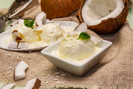 Lactose free coconut ice cream. Special spoon, halves of fruit, flakes. Vegan dessert concept. Light green backgroundの写真素材