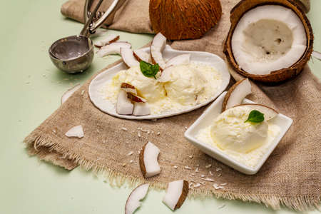 Lactose free coconut ice cream. Special spoon, halves of fruit, flakes. Vegan dessert concept. Light green backgroundの写真素材